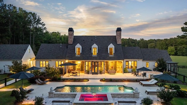 back of property at dusk featuring a chimney, a patio area, and a pool with connected hot tub