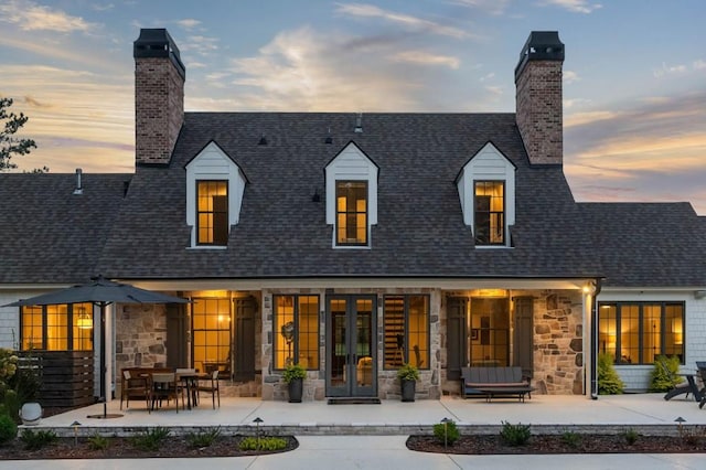 rear view of property featuring a chimney, french doors, and stone siding