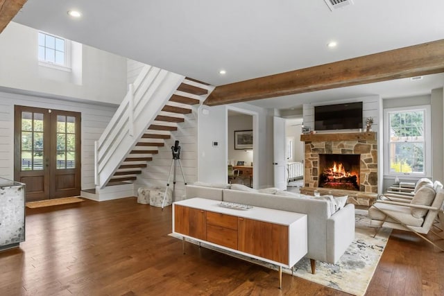 living room featuring stairway, dark wood-style floors, beamed ceiling, a stone fireplace, and recessed lighting