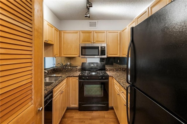 kitchen featuring dark stone counters, light brown cabinets, a textured ceiling, and black appliances