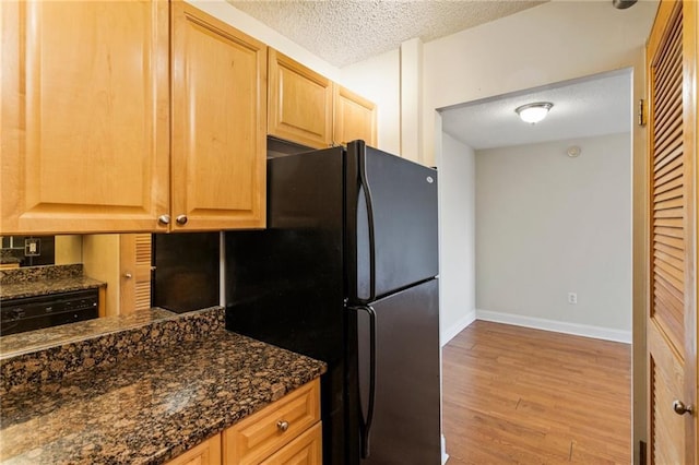 kitchen with black refrigerator, light hardwood / wood-style flooring, dark stone counters, and a textured ceiling