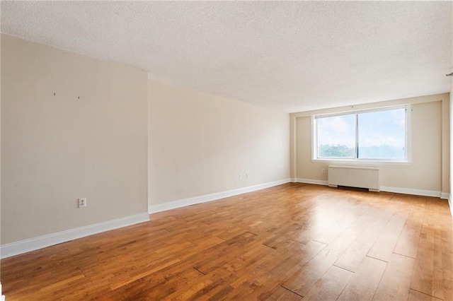 empty room with radiator, light hardwood / wood-style flooring, and a textured ceiling