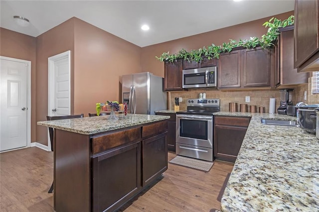 kitchen with stainless steel appliances, light wood-style floors, backsplash, and dark brown cabinetry