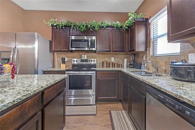 kitchen with tasteful backsplash, light wood-style flooring, appliances with stainless steel finishes, a sink, and light stone countertops