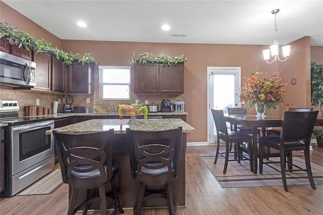 kitchen with stainless steel appliances, a center island, light wood-style flooring, and decorative backsplash