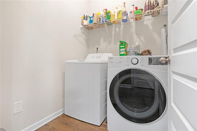 washroom featuring washing machine and dryer, laundry area, baseboards, and wood finished floors