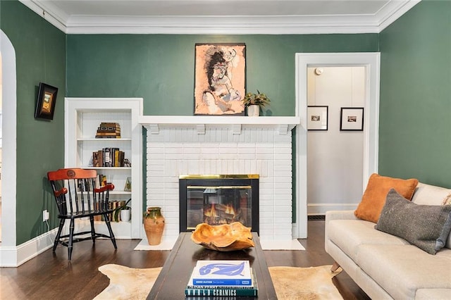 living room featuring built in shelves, ornamental molding, a fireplace, and dark wood-type flooring