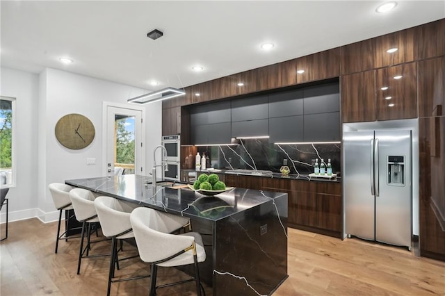 kitchen with an island with sink, stainless steel appliances, tasteful backsplash, and light hardwood / wood-style flooring