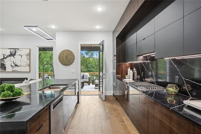 kitchen with sink, dark brown cabinets, backsplash, appliances with stainless steel finishes, and light wood-type flooring