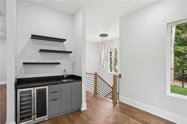 bar featuring dark wood-type flooring, beverage cooler, sink, and gray cabinetry