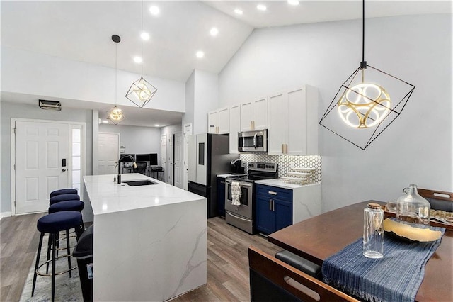 kitchen with sink, blue cabinetry, appliances with stainless steel finishes, a center island with sink, and decorative light fixtures