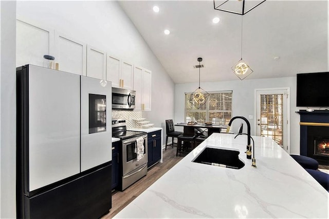 kitchen featuring sink, decorative backsplash, hanging light fixtures, light stone counters, and stainless steel appliances