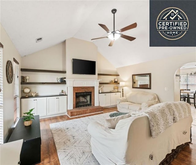 living area featuring arched walkways, a fireplace, visible vents, vaulted ceiling, and wood finished floors