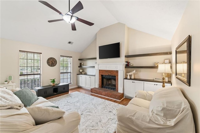 living room with visible vents, a ceiling fan, wood finished floors, vaulted ceiling, and a brick fireplace