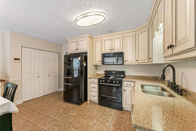 kitchen with cream cabinets, light tile patterned flooring, a sink, a textured ceiling, and black appliances