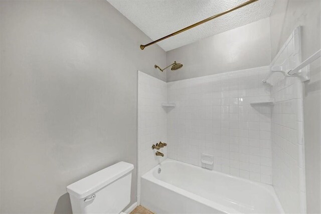 bathroom featuring a textured ceiling, toilet, and tiled shower / bath combo