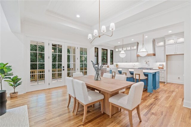 dining room featuring light wood-style floors, a raised ceiling, ornamental molding, recessed lighting, and french doors