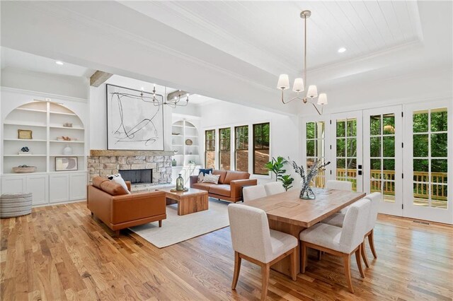 dining area with a chandelier, light wood finished floors, ornamental molding, a fireplace, and built in features