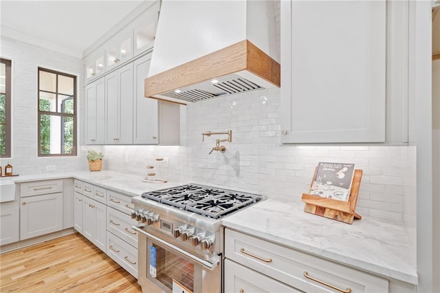 kitchen featuring high end stainless steel range oven, premium range hood, tasteful backsplash, light stone countertops, and ornamental molding
