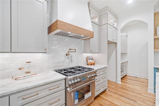 kitchen featuring high end stove, premium range hood, light stone countertops, arched walkways, and glass insert cabinets