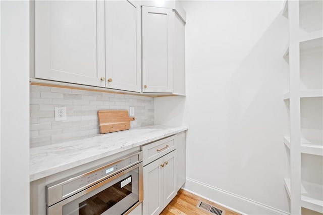 bar with stainless steel microwave, tasteful backsplash, light wood-style floors, and baseboards