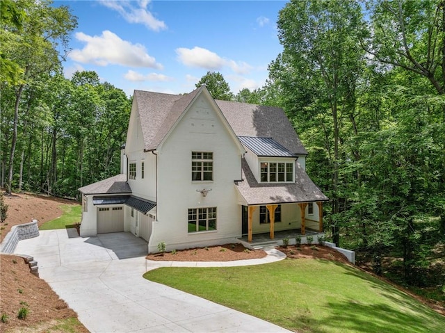 view of front of home with concrete driveway, covered porch, a front lawn, a standing seam roof, and roof with shingles