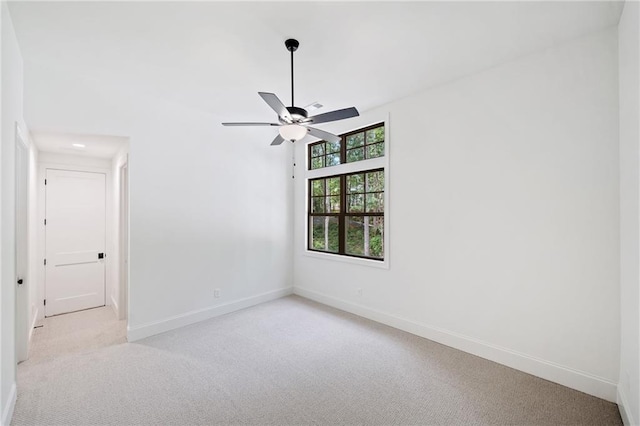 spare room featuring light carpet, a ceiling fan, and baseboards