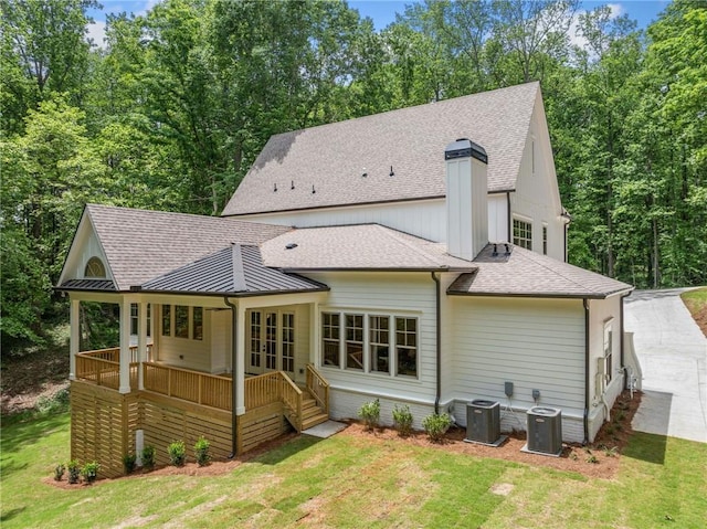 back of property with a shingled roof, a lawn, central AC, and a standing seam roof