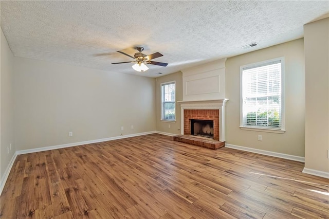 unfurnished living room featuring ceiling fan, a fireplace, light hardwood / wood-style floors, and a textured ceiling