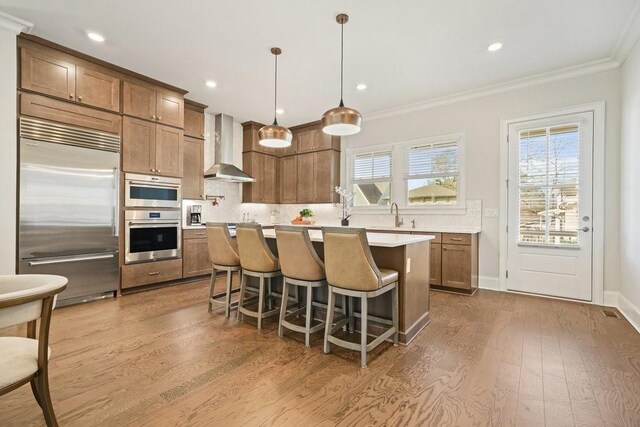 kitchen with decorative light fixtures, a breakfast bar area, light countertops, appliances with stainless steel finishes, and wall chimney exhaust hood