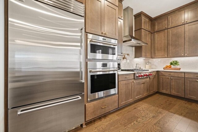 kitchen featuring light countertops, backsplash, appliances with stainless steel finishes, dark wood-type flooring, and wall chimney exhaust hood