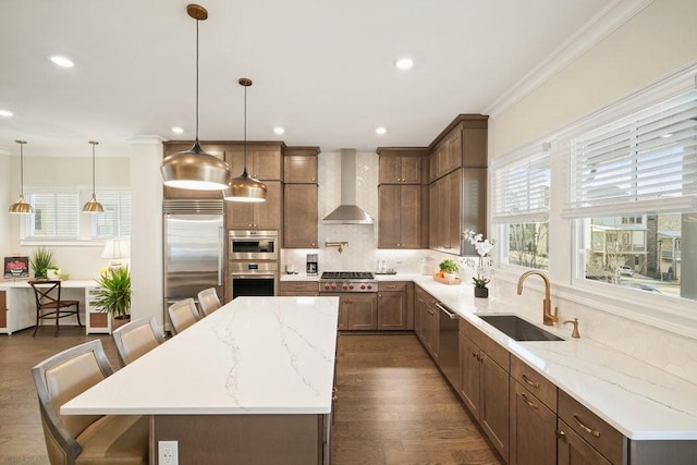 kitchen with wall chimney range hood, a sink, appliances with stainless steel finishes, a center island, and dark wood-style floors