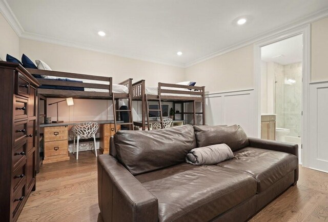 bedroom featuring ornamental molding, wainscoting, wood finished floors, and a decorative wall