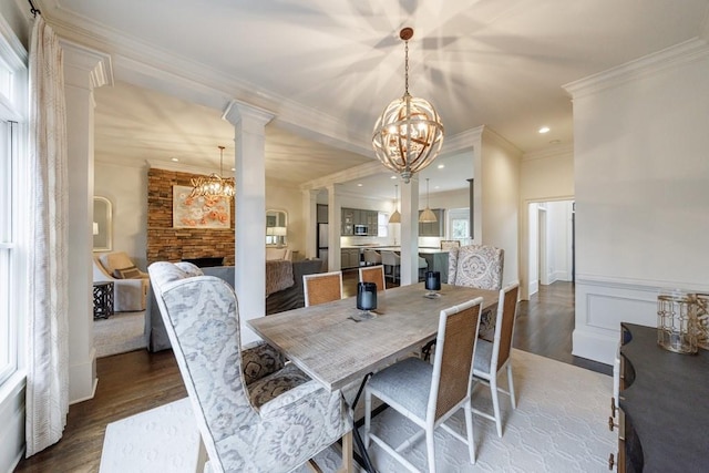 dining room with wood finished floors, crown molding, ornate columns, and an inviting chandelier