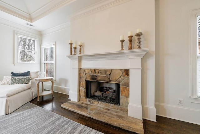 living area featuring ornamental molding, visible vents, a stone fireplace, and wood finished floors