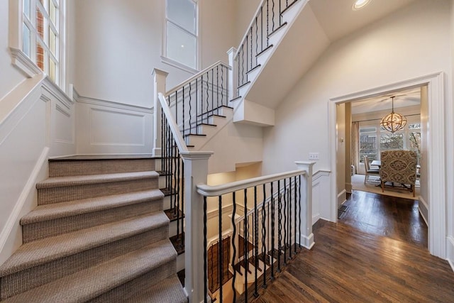 staircase with a wainscoted wall, a high ceiling, a decorative wall, and wood finished floors