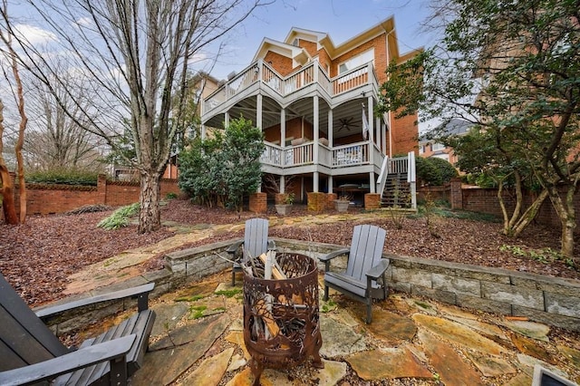 back of property featuring a balcony, a fire pit, brick siding, fence, and stairs