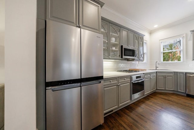 kitchen with a sink, appliances with stainless steel finishes, ornamental molding, gray cabinets, and dark wood-style floors