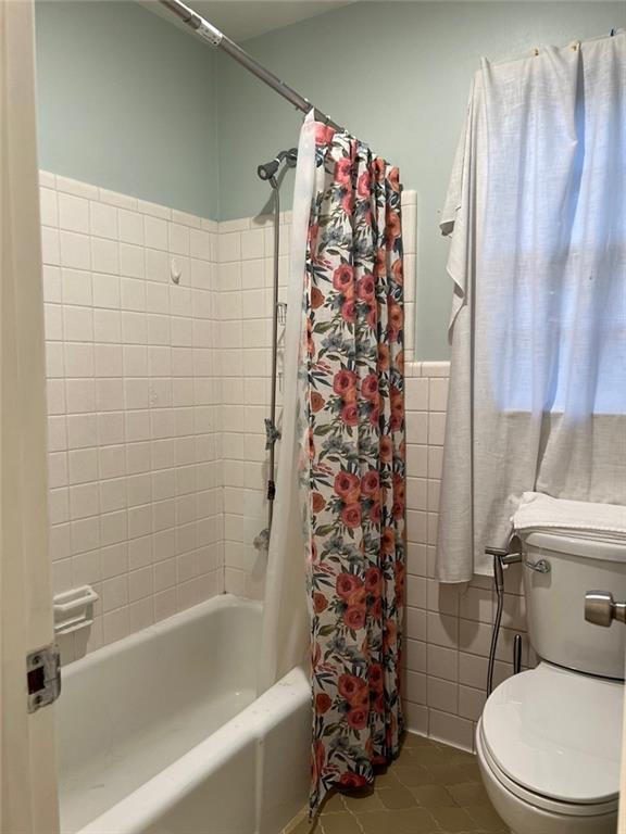 1017 Clifton Dr, Macon, GA 31204 - full bathroom featuring tile patterned floors, shower / tub combo with curtain, toilet, tile walls, and wainscoting