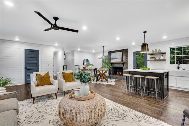 living room with light wood-type flooring, sink, a fireplace, crown molding, and ceiling fan