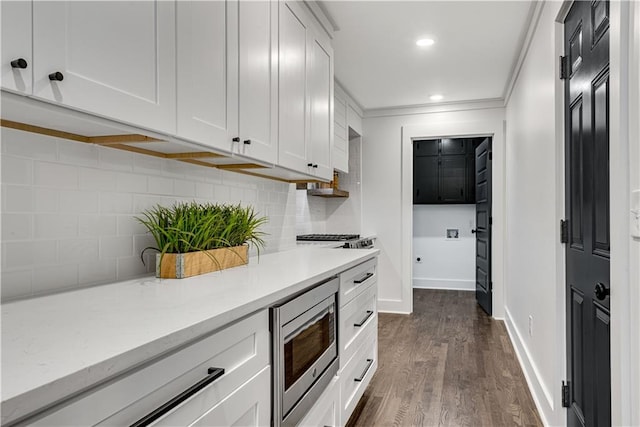 kitchen featuring dark hardwood / wood-style flooring, tasteful backsplash, white cabinetry, stainless steel microwave, and crown molding