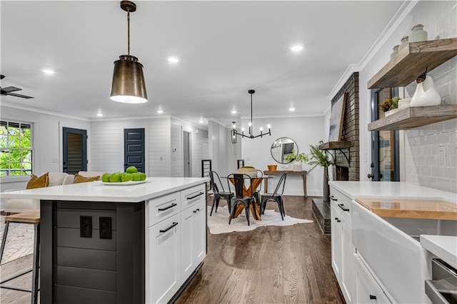 kitchen featuring ornamental molding, a kitchen island, decorative light fixtures, white cabinetry, and dark hardwood / wood-style flooring