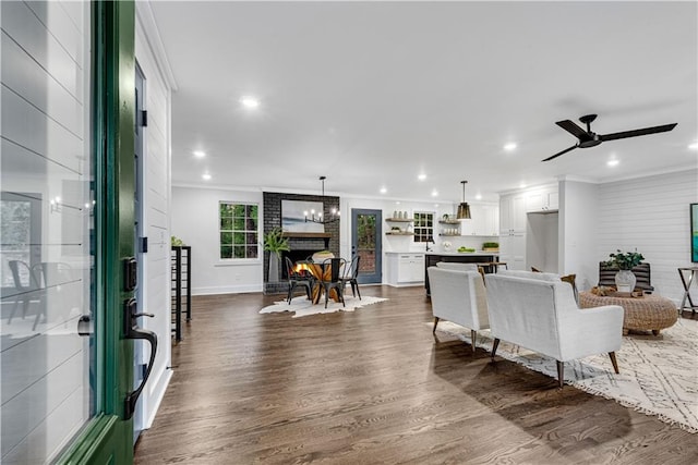 living room with a fireplace, ornamental molding, ceiling fan, and dark wood-type flooring