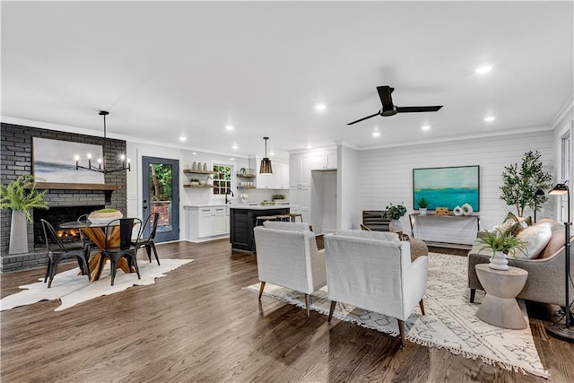 living room with ceiling fan, sink, a brick fireplace, dark hardwood / wood-style floors, and crown molding