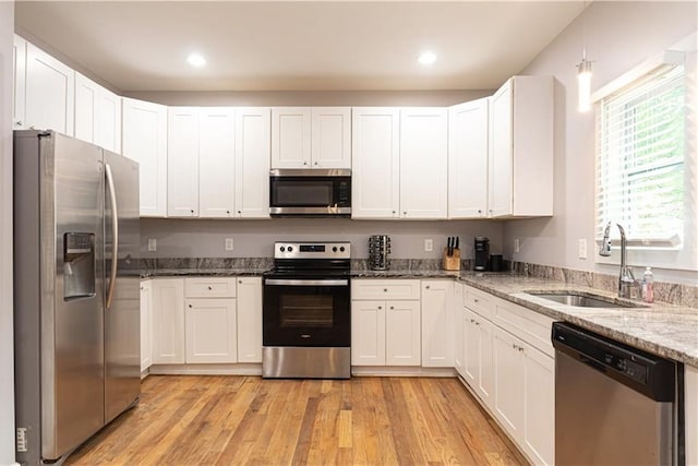kitchen featuring light stone counters, a sink, light wood finished floors, stainless steel appliances, and white cabinetry