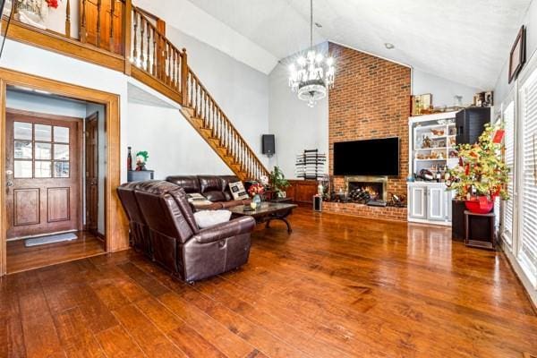 living room featuring a notable chandelier, wood-type flooring, a fireplace, and high vaulted ceiling