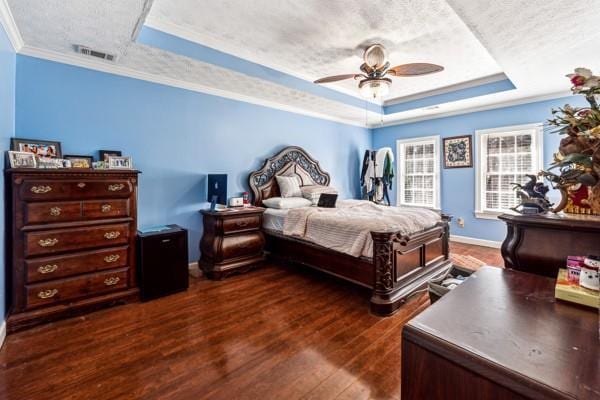 bedroom featuring dark hardwood / wood-style floors, ornamental molding, a raised ceiling, and a textured ceiling