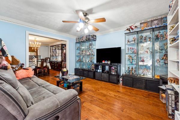 living room featuring wood-type flooring, ornamental molding, and ceiling fan with notable chandelier