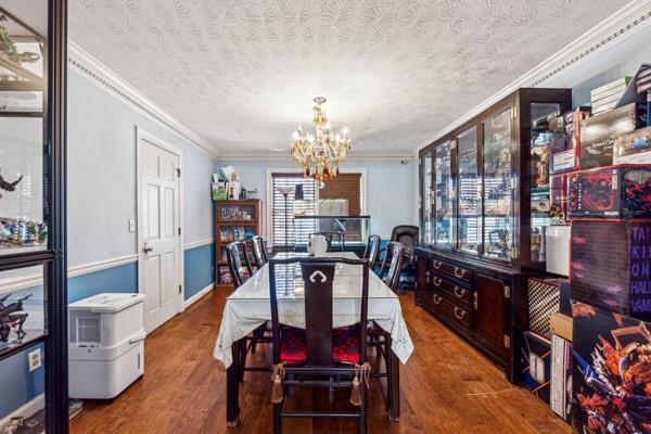 dining area featuring wood-type flooring, ornamental molding, a notable chandelier, and a textured ceiling