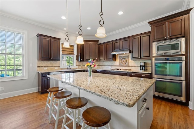 kitchen featuring a kitchen island, stainless steel appliances, dark brown cabinetry, and a healthy amount of sunlight